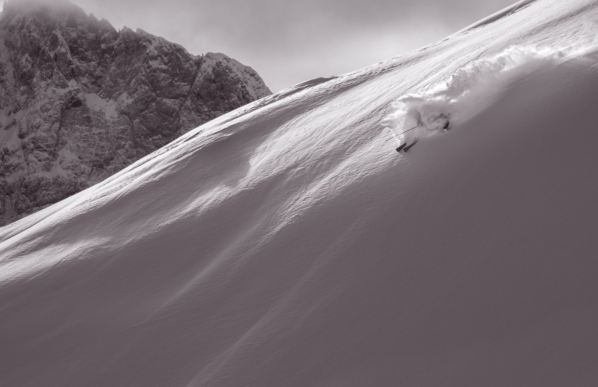 Black and white skier carving powder on a rugged mountain ridge