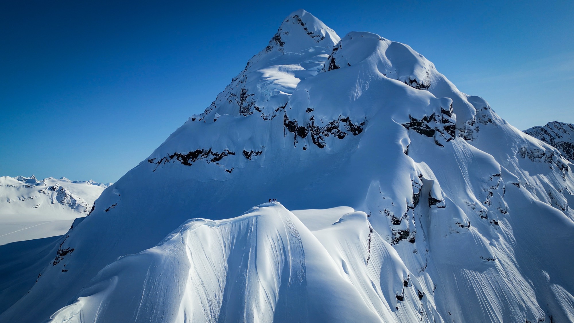 Four tiny skiers on the crest of a huge snow-covered peak