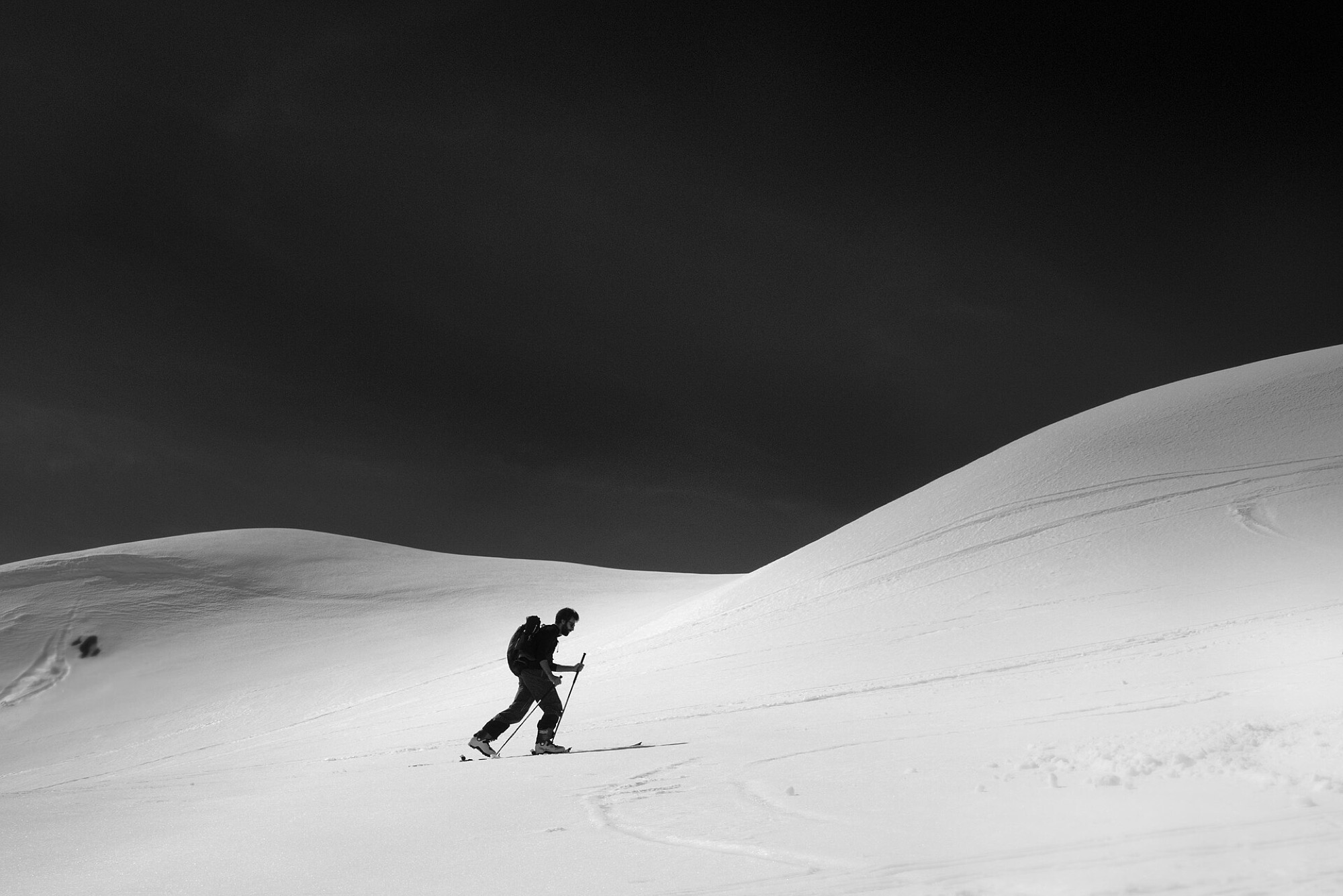 Lone ski tourer skinning up a snow ridge under a dark sky